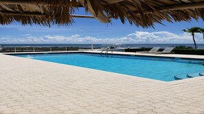 A swimming pool with a view of the ocean, surrounded by hexagonal tiles and a thatched roof.