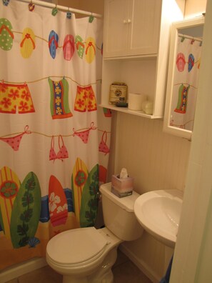 Une salle de bain équipée de toilettes, d’un lavabo et d’un rideau de douche orné d’un motif de planche de surf.