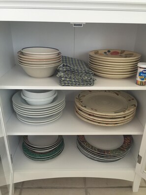 Une étagère blanche comportant plusieurs piles d’assiettes et de bols, dont certains sont ornés de motifs décoratifs.