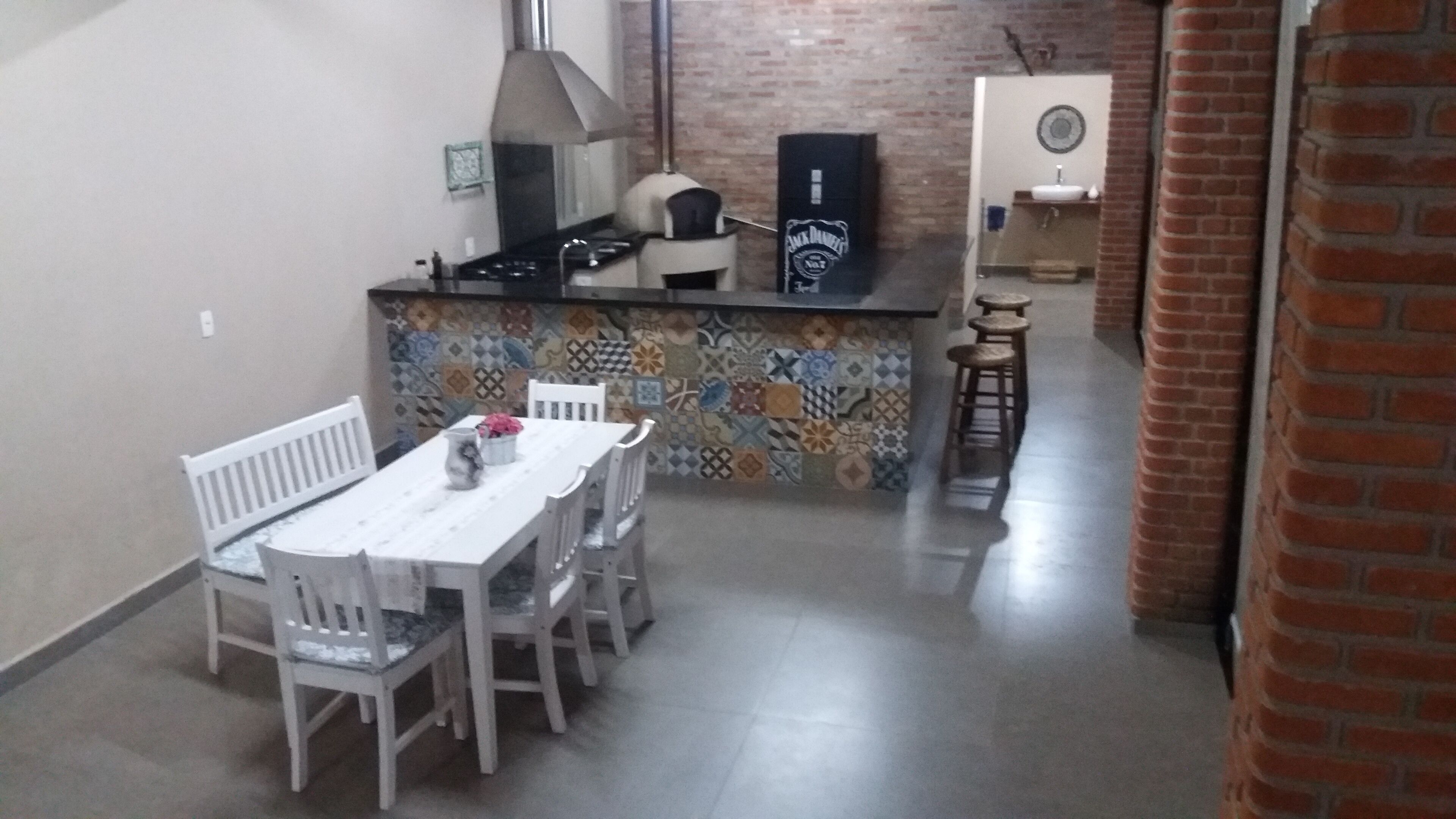 A kitchen with a tiled backsplash, a stove, and a sink. There is a dining table with chairs and a small bar area with stools.