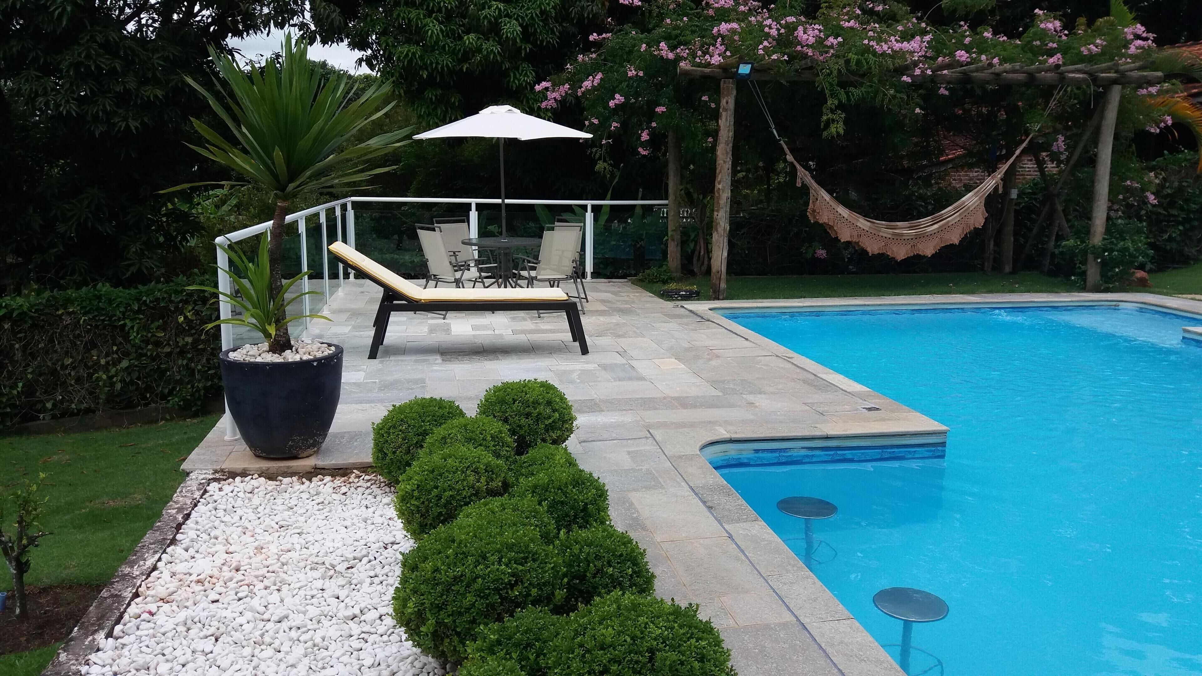 Una piscina con bordo piastrellato, una sedia a sdraio, una pianta in vaso e un'amaca.