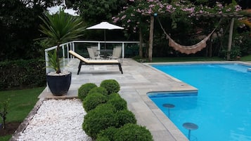 Una piscina con bordo piastrellato, una sedia a sdraio, una pianta in vaso e un'amaca.
