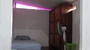 Una stanza modesta con un letto, una ventola e un armadio in legno.