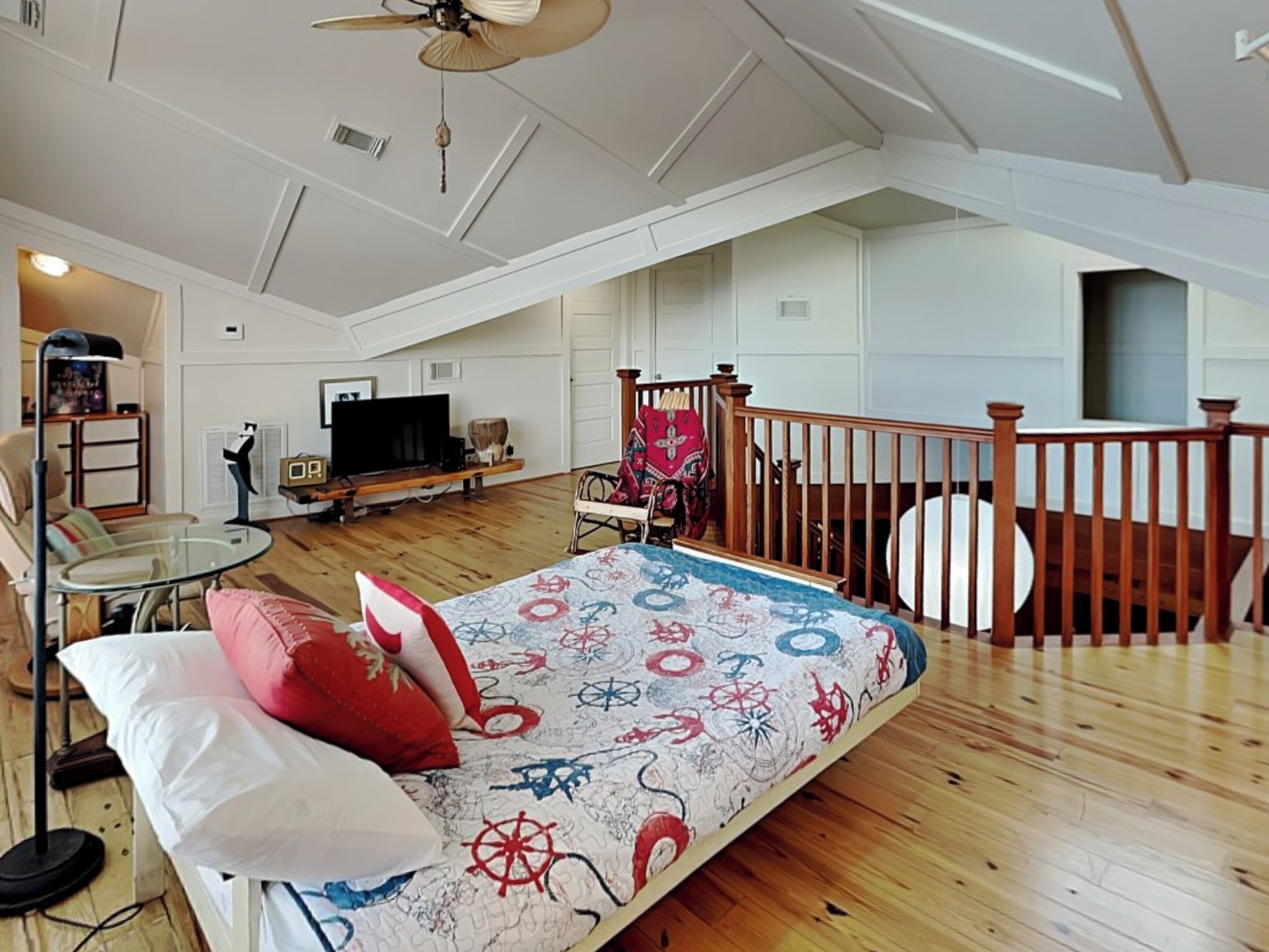 Ein geräumiges Schlafzimmer im Loft-Stil mit einem großen Bett, einem hölzernen Deckenventilator, einem Fernseher und einer gemütlichen Sitzecke mit einem Sessel und einem kleinen Tisch.