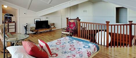 Ein geräumiges Schlafzimmer im Loft-Stil mit einem großen Bett, einem hölzernen Deckenventilator, einem Fernseher und einer gemütlichen Sitzecke mit einem Sessel und einem kleinen Tisch.