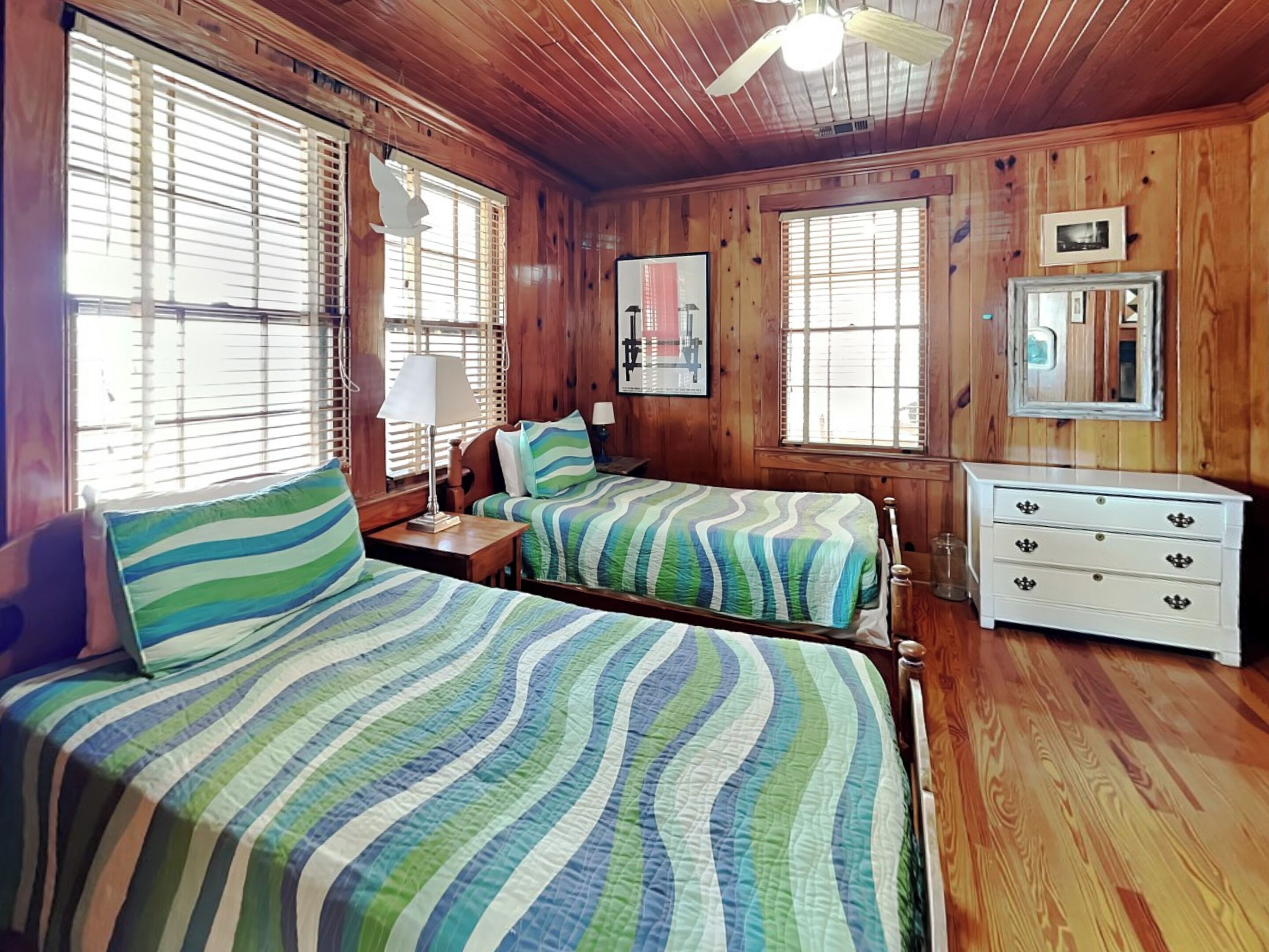 A wooden cabin bedroom with two beds, a dresser, and a ceiling fan.