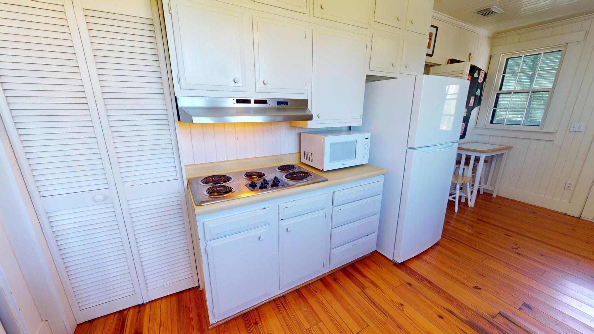 A compact kitchen with white cabinets, a stove, a microwave, and a refrigerator.