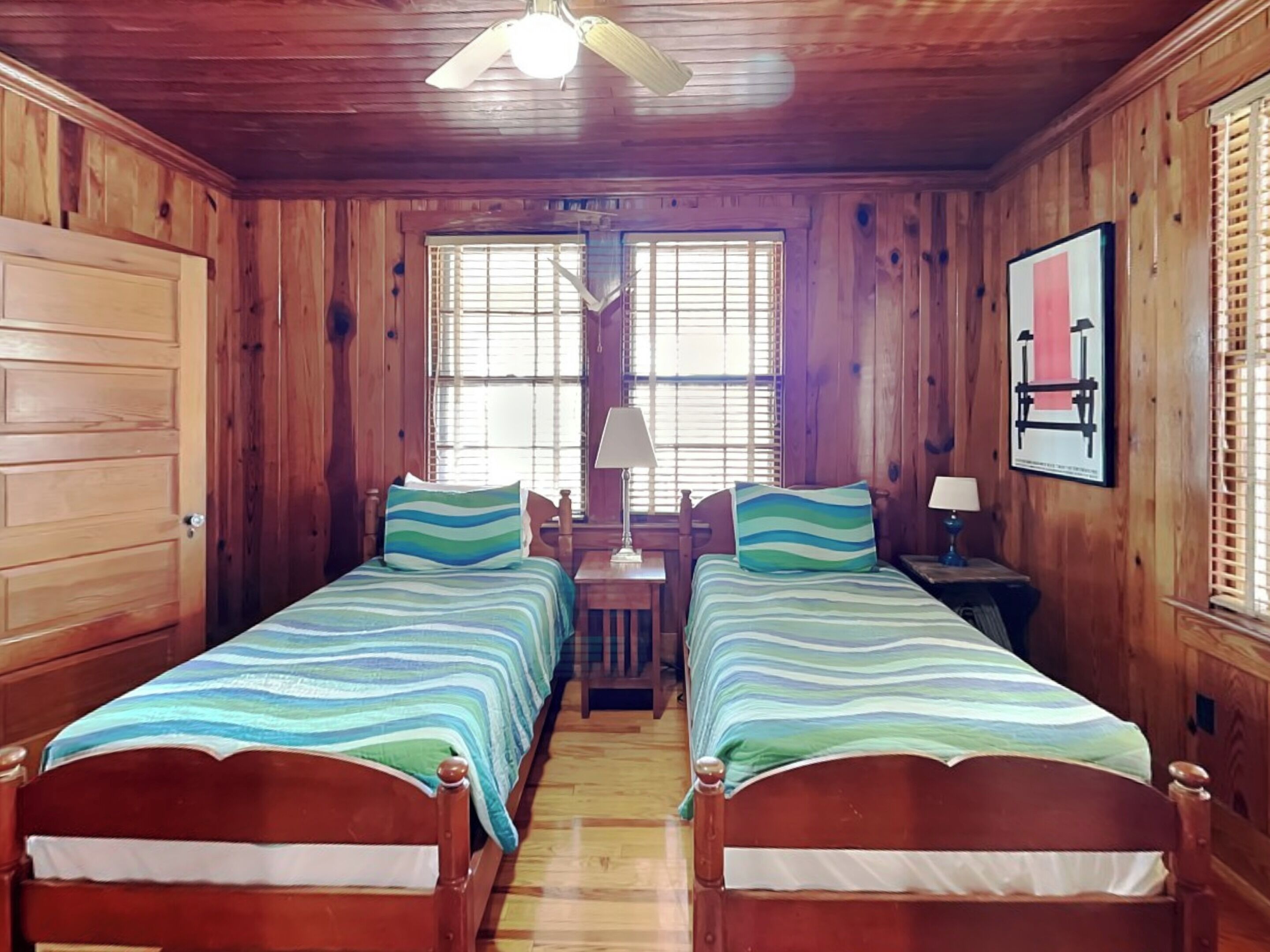 A wooden room with two beds, a ceiling fan, and a window with blinds.