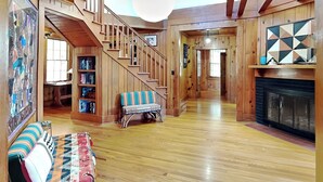A spacious living area with a wooden staircase, a fireplace, and a large window.