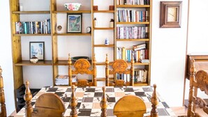 A room with a wooden bookshelf filled with books and decorative items, a chess table with a checkered tablecloth, and wooden chairs. - Frontline Apartment Great Views (Nerja)