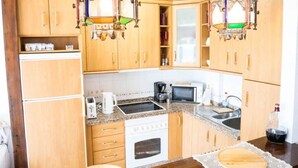 A kitchen with wooden cabinets, a stove, a microwave, and two hanging light fixtures. - Frontline Apartment Great Views (Nerja)