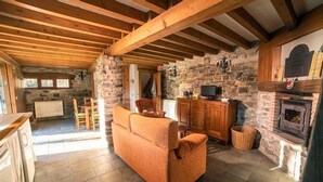 A cozy cabin interior with a stone wall, wooden beams, a sofa, a television, and a fireplace. - Rural house El Huerto de la Fragua for 5 people (Enciso)