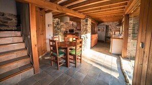 A rustic wooden interior with a stone fireplace, a dining area with wooden chairs, and a kitchen with stone walls. - Rural house El Huerto de la Fragua for 5 people (Enciso)