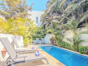 Relax by the serene pool surrounded by lush greenery and palm trees, with comfortable lounge chairs and a view of the surrounding foliage.