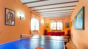 A room with a ping pong table, a red sofa, and a painting on the wall.