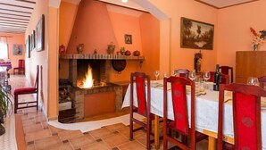 A dining area with a fireplace, wooden chairs, a table set for a meal, and a painting on the wall.