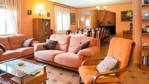 A living room with a sofa, armchair, and coffee table. There is a dining area in the background with a table set for a meal.