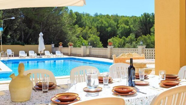 A dining area with a pool view, white chairs, and a table set for two with plates, glasses, and a bottle.