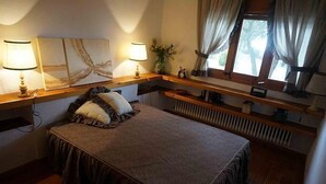 A bedroom with a bed, two bedside lamps, a window with curtains, and a radiator. - Self catering La Roureda for 9 people (Àger)
