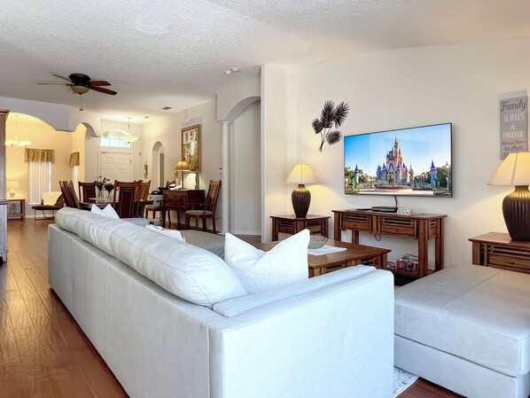 Uma sala de estar moderna com um sofá, uma televisão exibindo um castelo e um espaço de jantar com cadeiras e uma mesa.