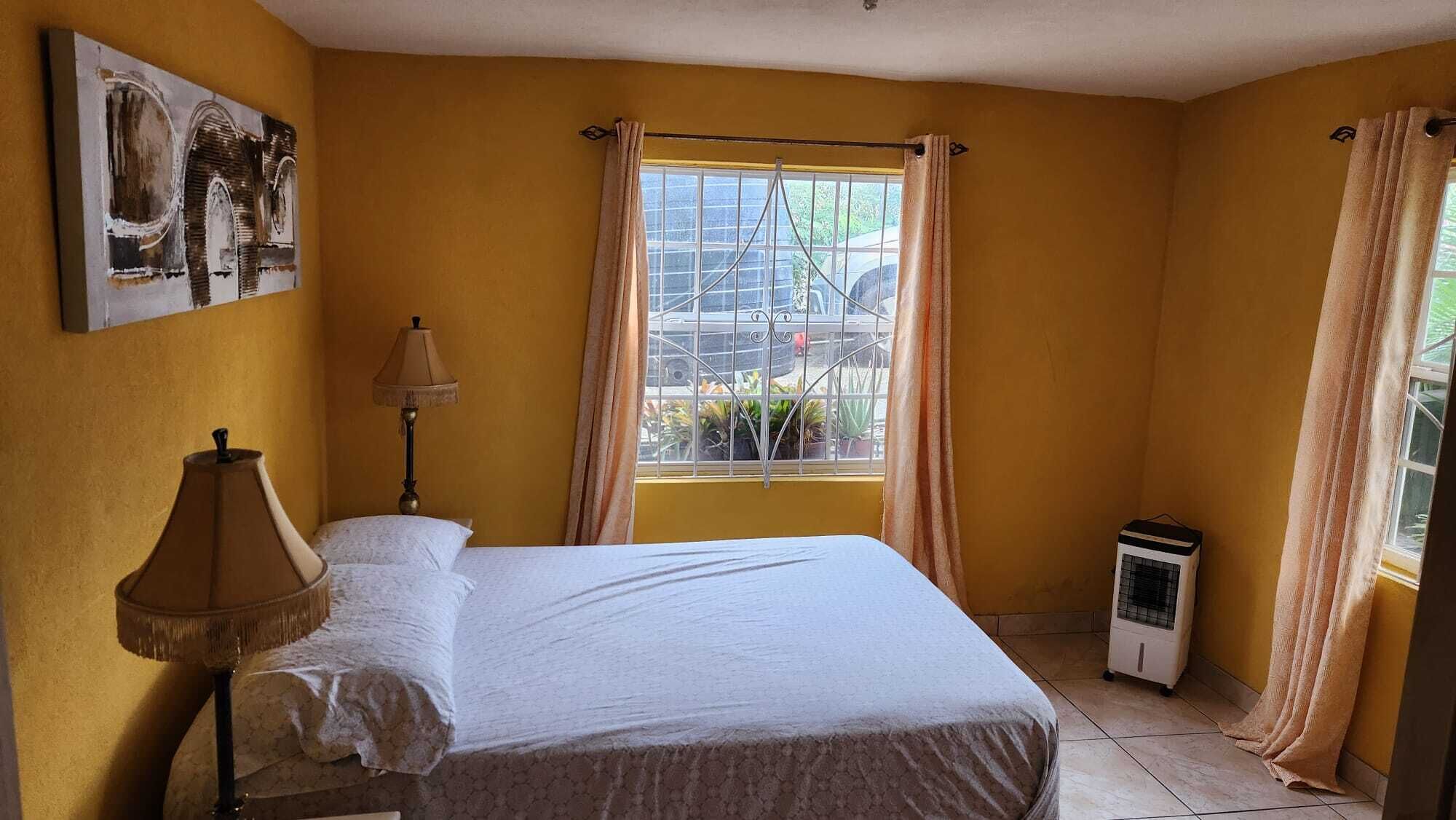 A bedroom with a bed, a lamp, a window with curtains, a radiator, and a painting on the wall.