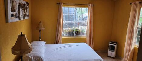 A bedroom with a bed, a lamp, a window with curtains, a radiator, and a painting on the wall.