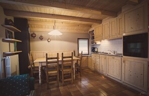 Een keuken met houten kastjes, een eettafel met stoelen, een hanglamp en een inbouwoven.