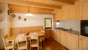 Una cucina con mobili in legno, un tavolo da pranzo con sedie, una lampada a sospensione e una finestra vista verde.