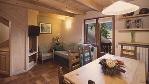 Un soggiorno accogliente con soffitto in legno, un divano a quadri, un tavolo da pranzo con un vaso di fiori e una televisione su uno scaffale.