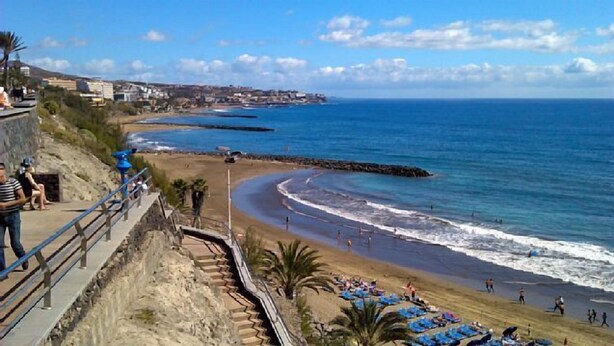 Una playa costera con un litoral rocoso, un paseo marítimo y sombrillas de playa.