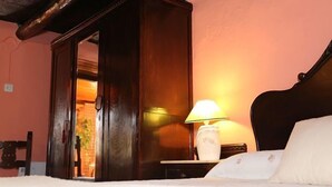 Una habitación de hotel con un armario de madera, una mesita de noche con lámpara y una cama con ropa de cama blanca.