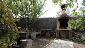 Un sendero de piedra conduce a un horno rústico al aire libre, rodeado de macetas de madera y una valla de madera.