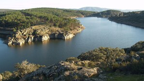 Um rio serpenteia por uma paisagem arborizada, com afloramentos rochosos e colinas ao fundo.