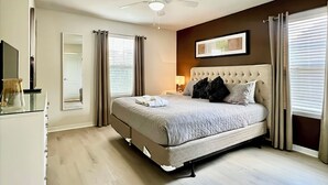 Een slaapkamer met een bed, een plafondventilator, een nachtkastje, een lamp en een raam met jaloezieën.