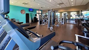 Een sportschool met loopbanden, gewichtstoestellen en een klok aan de muur.
