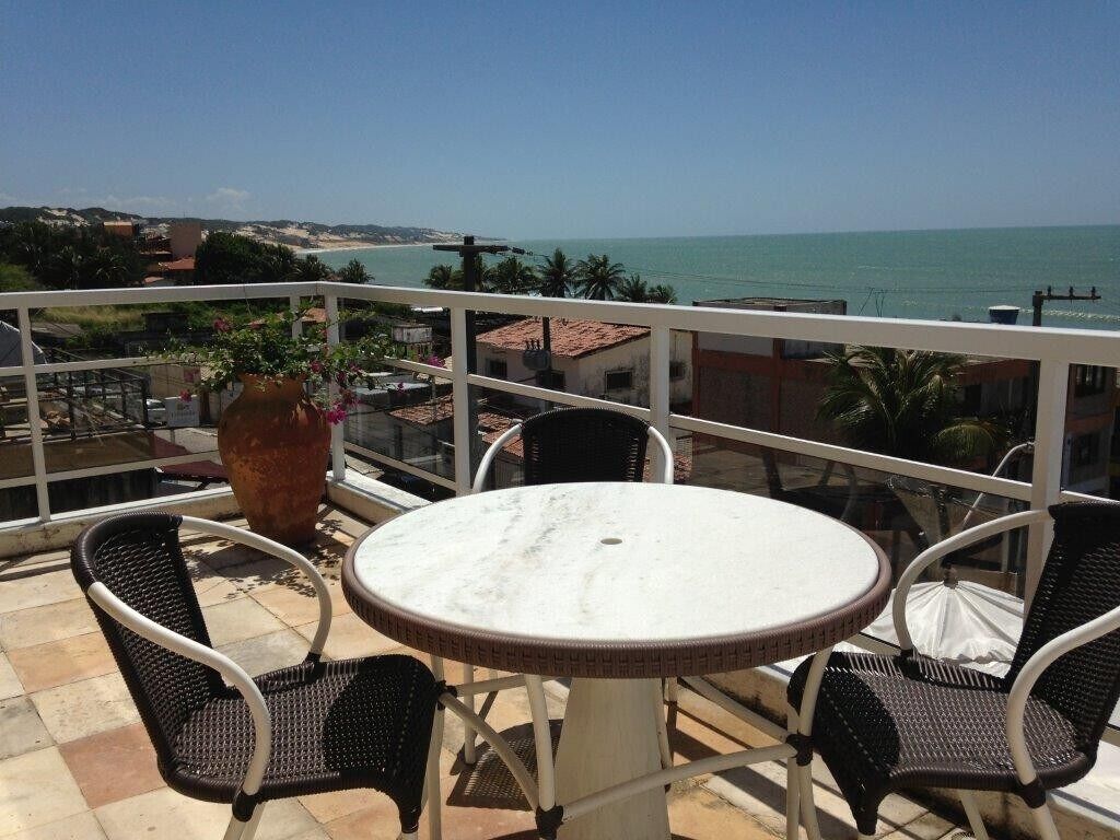 Un balcón con una mesa redonda y cuatro sillas, con vista a una playa y el océano.