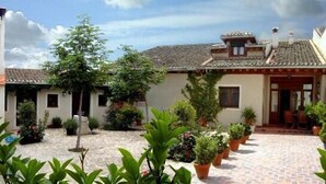 Une cour avec des plantes en pot, un sol carrelé et un bâtiment doté d’un toit en tuiles.