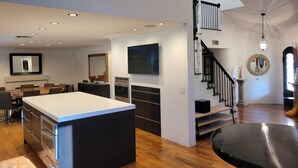 Une cuisine moderne dotée d’un îlot central, d’un coin repas avec une longue table et d’un escalier menant à l’étage supérieur.