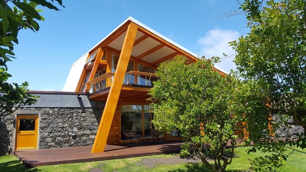 Une maison moderne avec des fondations en pierre, un balcon en bois et une cour verdoyante.