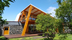Una casa moderna amb fonaments de pedra, un balcó de fusta i un jardí amb gespa.