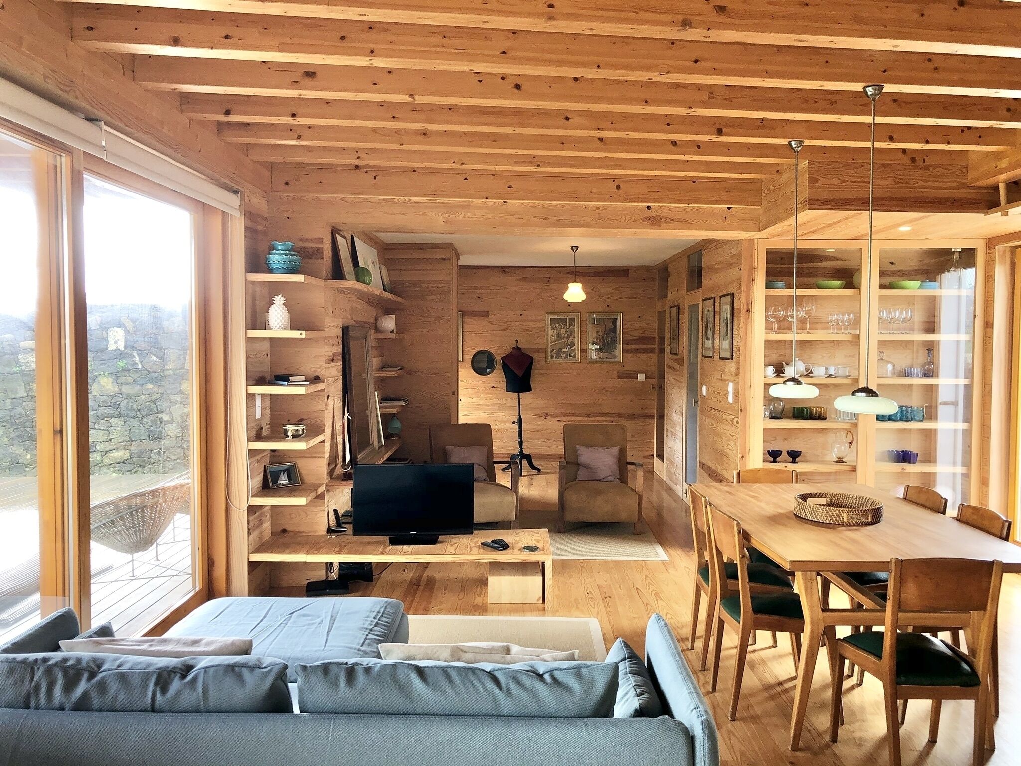 L’intérieur d’un chalet accueillant, avec un plafond en bois, un canapé, un téléviseur, une table à manger et des étagères remplies de divers objets.