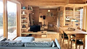 L’intérieur d’un chalet accueillant, avec un plafond en bois, un canapé, un téléviseur, une table à manger et des étagères remplies de divers objets.