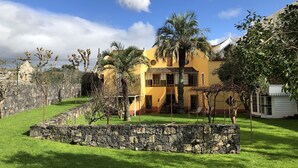 Une maison jaune avec un mur en pierre et un palmier dans la cour.