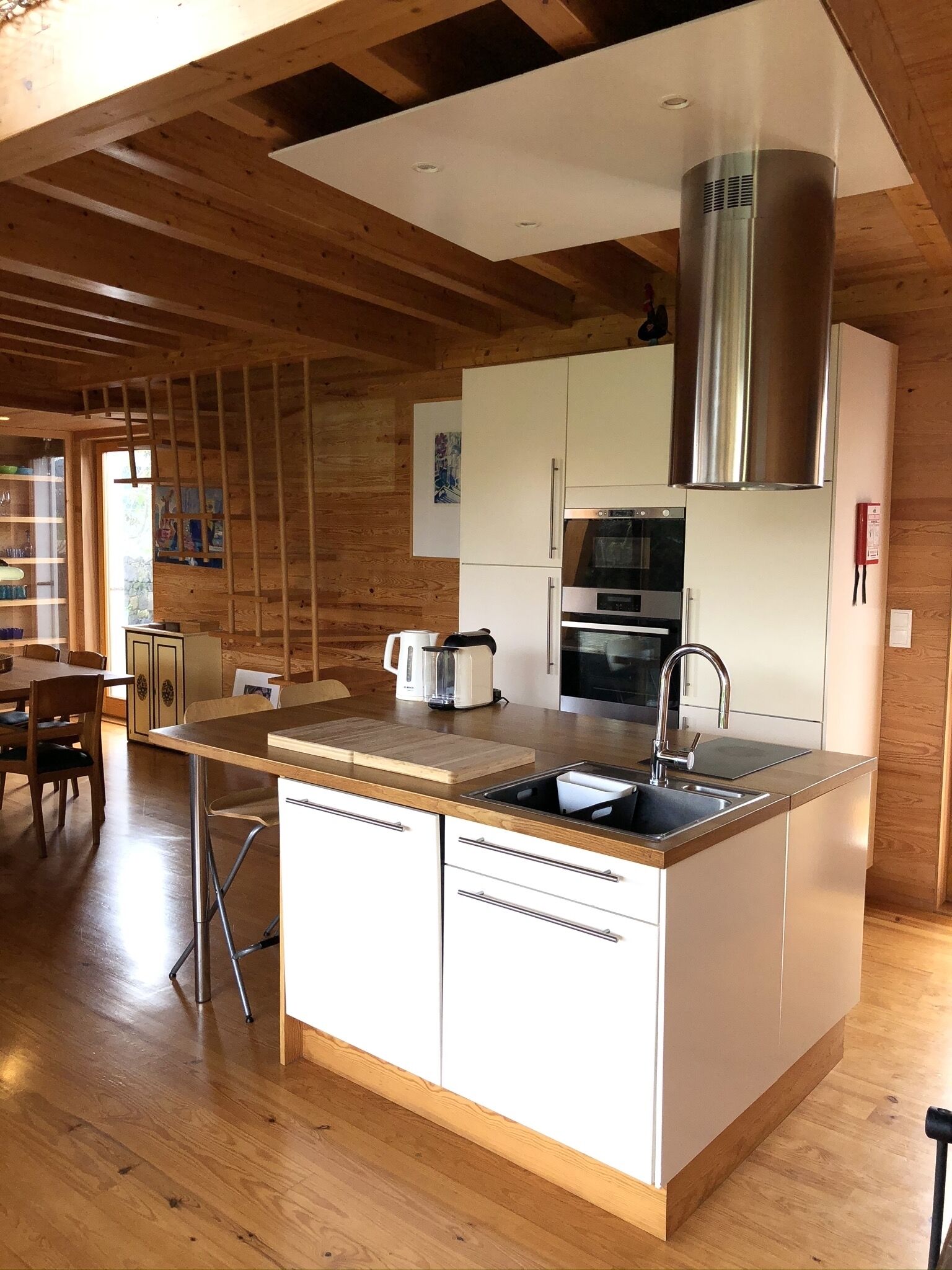 Une cuisine moderne avec des poutres en bois, un îlot central doté d’un évier, d’une cuisinière et d’une grande hotte en acier inoxydable.