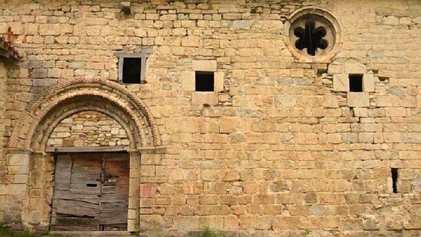 A stone building with an arched entrance, a circular window, and small rectangular windows.