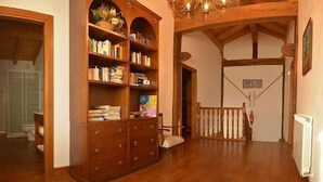 A spacious room with wooden floors, a large wooden bookshelf, a chandelier, and a staircase leading to another level.