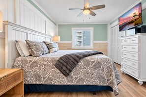 Een slaapkamer met een bed, een plafondventilator, een dressoir en een raam met jaloezieën.