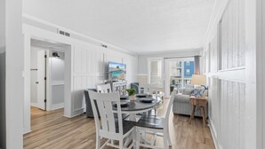 Een moderne keuken met witte kasten, een eethoek met een ronde tafel en stoelen, en een uitzicht op een stadsbeeld door het raam.