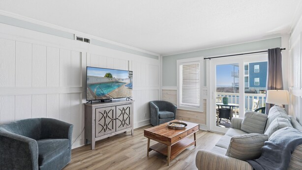 Een moderne woonkamer met een flatscreen televisie, een houten salontafel en een bank. Er is uitzicht op een balkon met een hekwerk en een gebouw op de achtergrond.