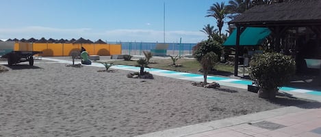 A beach area with a sandy walkway, a small pool, and a gazebo.
